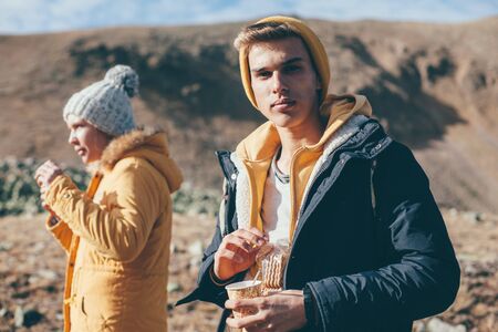 Teen guy drinking tea or coffee in mountains with friends. Young backpackers enjoying winter journey.の写真素材