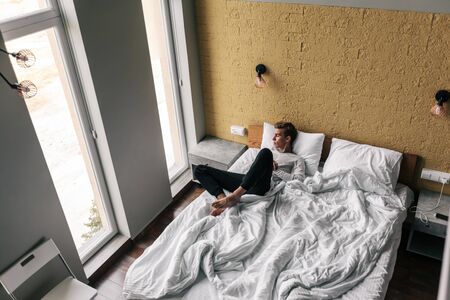 Young man sleeping on comfy bed in modern hotel roomの写真素材