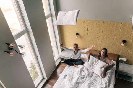 Young teen girl and guy relaxing and playing with pillows on comfy bed in modern hotel room, top viewの写真素材