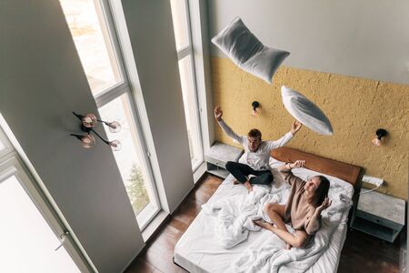 Young teen girl and guy relaxing and playing with pillows on comfy bed in modern hotel room, top viewの写真素材
