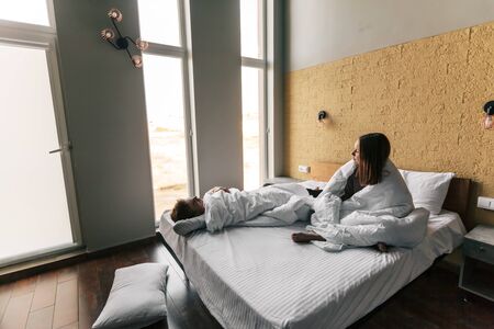 Young teen girl and guy relaxing on comfy bed and looking at window in modern hotel room, top viewの写真素材