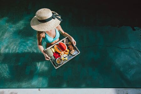 Girl relaxing and eating fruits in the pool on luxury villa in Bali. Exotic summer diet. Tropical...