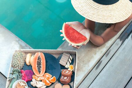 Girl relaxing and eating fruits in the pool on luxury villa in Bali. Exotic summer diet. Tropical beach lifestyle.の写真素材
