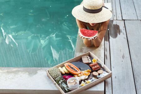Girl relaxing and eating fruits in the pool on luxury villa in Bali. Exotic summer diet. Tropical beach lifestyle.の写真素材