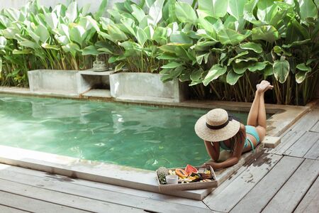 Girl relaxing and eating fruits in the pool on luxury villa in Bali. Exotic summer diet. Tropical beach lifestyle.の写真素材