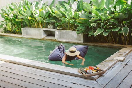 Girl relaxing and eating fruits in the pool on luxury villa in Bali. Exotic summer diet. Tropical beach lifestyle.の写真素材