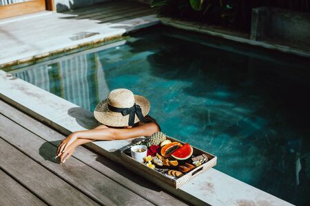 Girl relaxing and eating fruits in the pool on luxury villa in Bali. Exotic summer diet. Tropical beach lifestyle.の写真素材