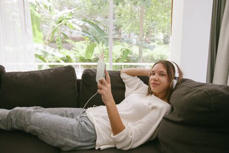 Teen girl using tablet pc while relaxing on couch in hotel room in front of big windowの写真素材