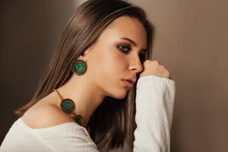 Fashion portrait of young beautiful girl with perfect smokey makeup wearing vintage jewelry. Teen model with elegant jewelery on brown background.の写真素材