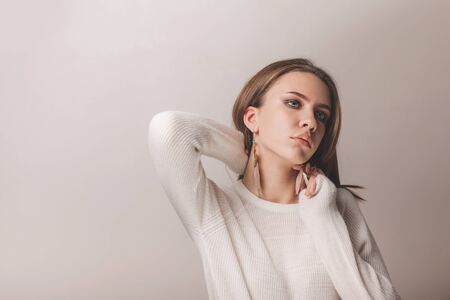 Natural studio portrait of beautiful teen girl with stylish makeup wearing cashmere sweater and feather earrings on light backgroundの写真素材