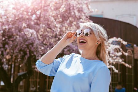 Beauitful plus size model wearing blue dress and trendy sunglasses smiling under pink blooming spring tree outdoor on the city street.の写真素材