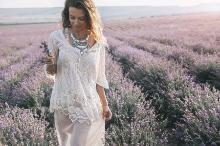 Beautiful model walking in spring or summer lavender field in sunrise sunshine. Boho style clothing...
