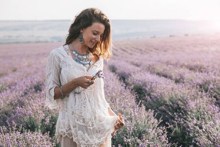 Beautiful model walking in spring or summer lavender field in sunrise sunshine. Boho style clothing and silver jewelry.の写真素材