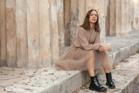Sepia filtered photo of teen girl wearing brown tulle skirt, knitted oversized sweater and leather boots posing in city street.の写真素材