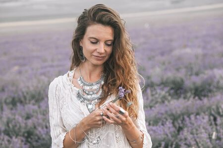 Beautiful model walking in spring or summer lavender field in sunrise backlit. Boho style clothing and jewelry.の写真素材