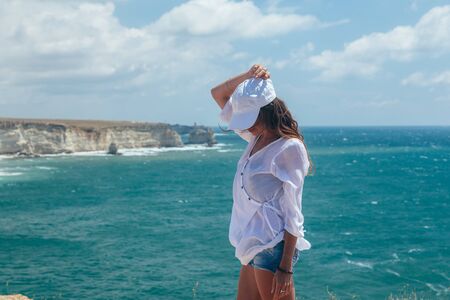 Back view of young traveller enjoying summer breeze while viewing beautiful sea landscapeの写真素材