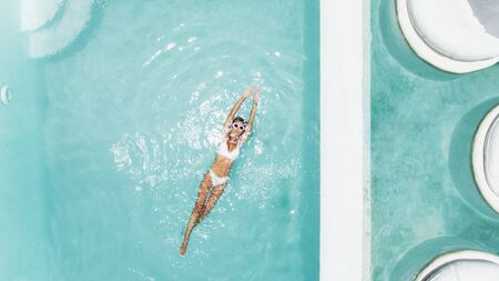 Woman relaxing in clear pool water in hot sunny day on Bali villa. Summer holiday idyllic, top view.の写真素材
