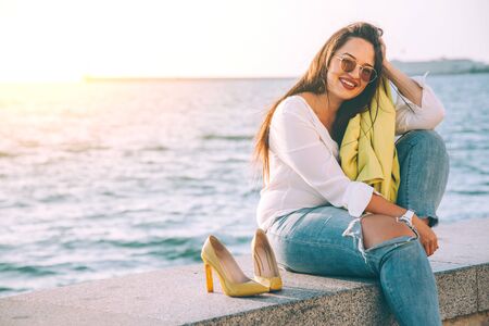 Carefree and happy plus size woman taking off her shoes, relaxing and enjoing sun light while walking on city streetの写真素材