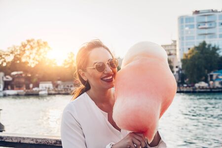 Happy plus size woman eating sugar cotton candy in city street. Smiling overweight lady enjoying sweet food while walking in park.の写真素材