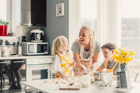 Beautiful blond mom teaching her two children cooking on the kitchen. Parent making everyday breakfast together with kids. Family at home lifestyle photo.の写真素材