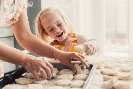 Beautiful blond mom teaching her daughter cooking on the kitchen. Parent making everyday breakfast together with child. Family at home lifestyle photo.の写真素材