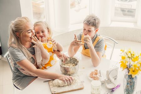 Beautiful blond mom teaching her two children cooking on the kitchen. Parent making everyday breakfast together with kids. Family at home lifestyle photo.の写真素材