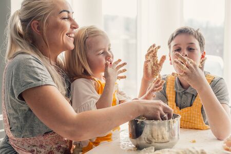 Beautiful blond mom teaching her two children cooking on the kitchen. Parent making everyday breakfast together with kids. Family at home lifestyle photo.の写真素材