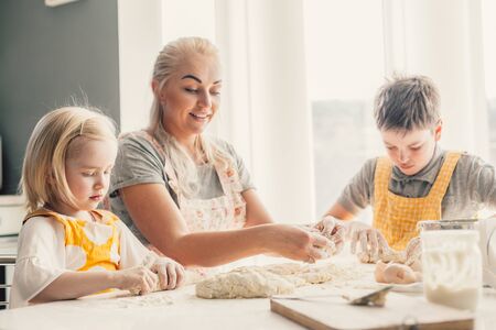 Beautiful blond mom teaching her two children cooking on the kitchen. Parent making everyday breakfast together with kids. Family at home lifestyle photo.の写真素材