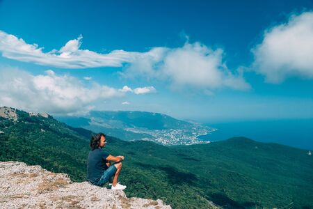Man traveler sitting on mountain top alone and looking at beautiful summer landscape and blue sea...