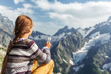 Back view of child girl hiker holiding spring flower and enjoying beautiful mountains landscapeの写真素材