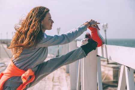 Fitness sport girl in fashion sportswear doing stretching exercise in the street. Outdoor workout in cold weather.の写真素材