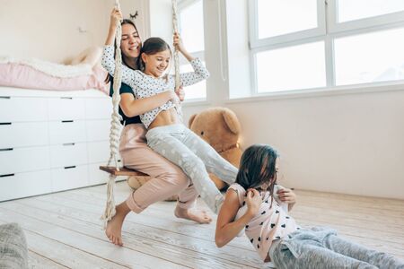 Group of children laughing and playing together, three girls having fun and swinging in bright scandinavian playroom. Kids paljamas party in white bedroom interior.の写真素材