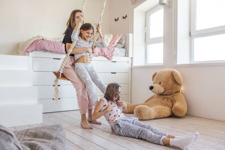 Group of children laughing and playing together, three girls having fun and swinging in bright scandinavian playroom. Kids paljamas party in white bedroom interior.の写真素材