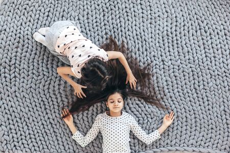 Children in sleepwear lying down and playing with each other on chunky giant woolen blanket, top viewの写真素材