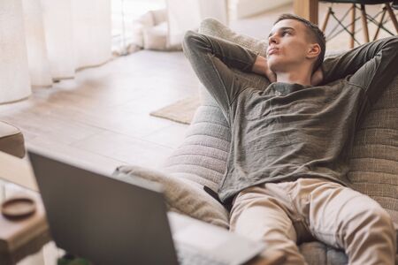 Handsome teenage guy relaxing on modern couch in living room interior. Young man resting in soft chair at home.の写真素材