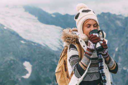 Child traveler with backpack drinking tea in flask mug in mountains with snow, winter hikingの写真素材
