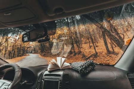 Fall trip looking inside of car. Book and knitted hat on windshield. Freedom travel concept. Autumn weekend to the forest.の写真素材