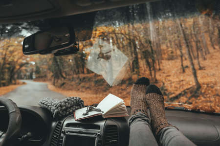Woman feet in warm socks on car dashboard. Fall trip. Looking through windshield. Freedom travel concept. Autumn weekend.の写真素材