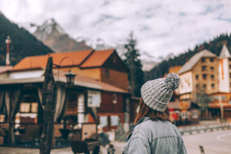 Teenage girl traveler standing and looking at village over mountains view. Student spending autumn...