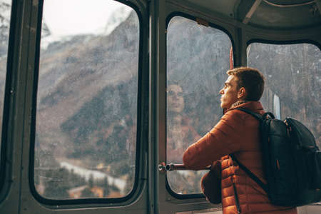 Young traveler with backpack looking at mountains view through sky lift window. Teenage guy spending his vacations in nordic country.の写真素材