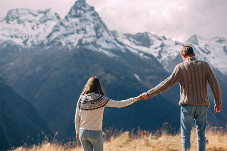 Two teenage friends dressed in warm fashion sweaters holding hands while walking in mountains enjoying beautiful landscape and feeling freedom and happiness. Autumn trip to nordic countries.の写真素材