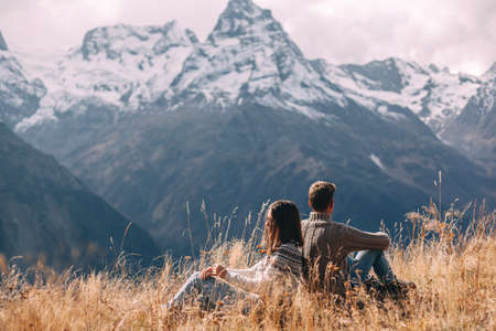 Two teenage friends dressed in warm fashion sweaters relaxing in mountains enjoying beautiful landscape and feeling freedom and happiness. Autumn trip to nordic countries.の写真素材