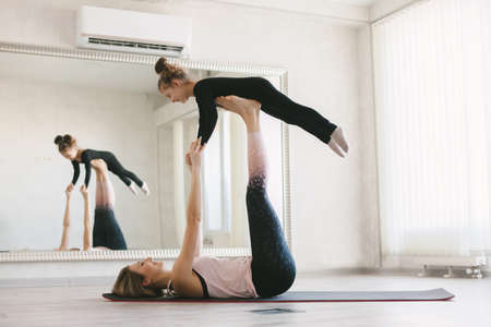 Beautiful sporty woman and little child girl doing together stretching exercise on yoga mat in front of mirror in fitness classの写真素材