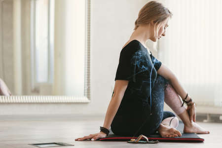 Young woman using aroma sticks while doing stretching exercise by mirror on floor mat in bright yoga class room.の写真素材