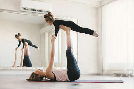 Beautiful sporty woman and little child girl doing together stretching exercise on yoga mat in front of mirror in fitness classの写真素材