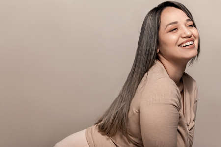 Beautiful and pretty plus size model with long colored glossy hair posing on beige studio background.の写真素材
