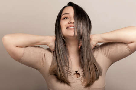 Beautiful and pretty plus size model with long colored glossy hair posing on beige studio background.の写真素材