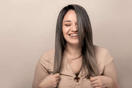 Beautiful and pretty plus size model with long colored glossy hair posing on beige studio background.の写真素材