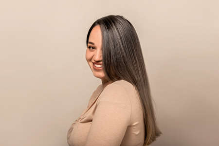 Beautiful and pretty plus size model with long colored glossy hair posing on beige studio background.の写真素材