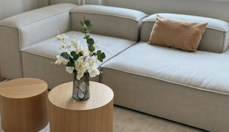Bouquet of artificial flowers in a vase on a round wooden table near sofa, fake plant living room decorの写真素材